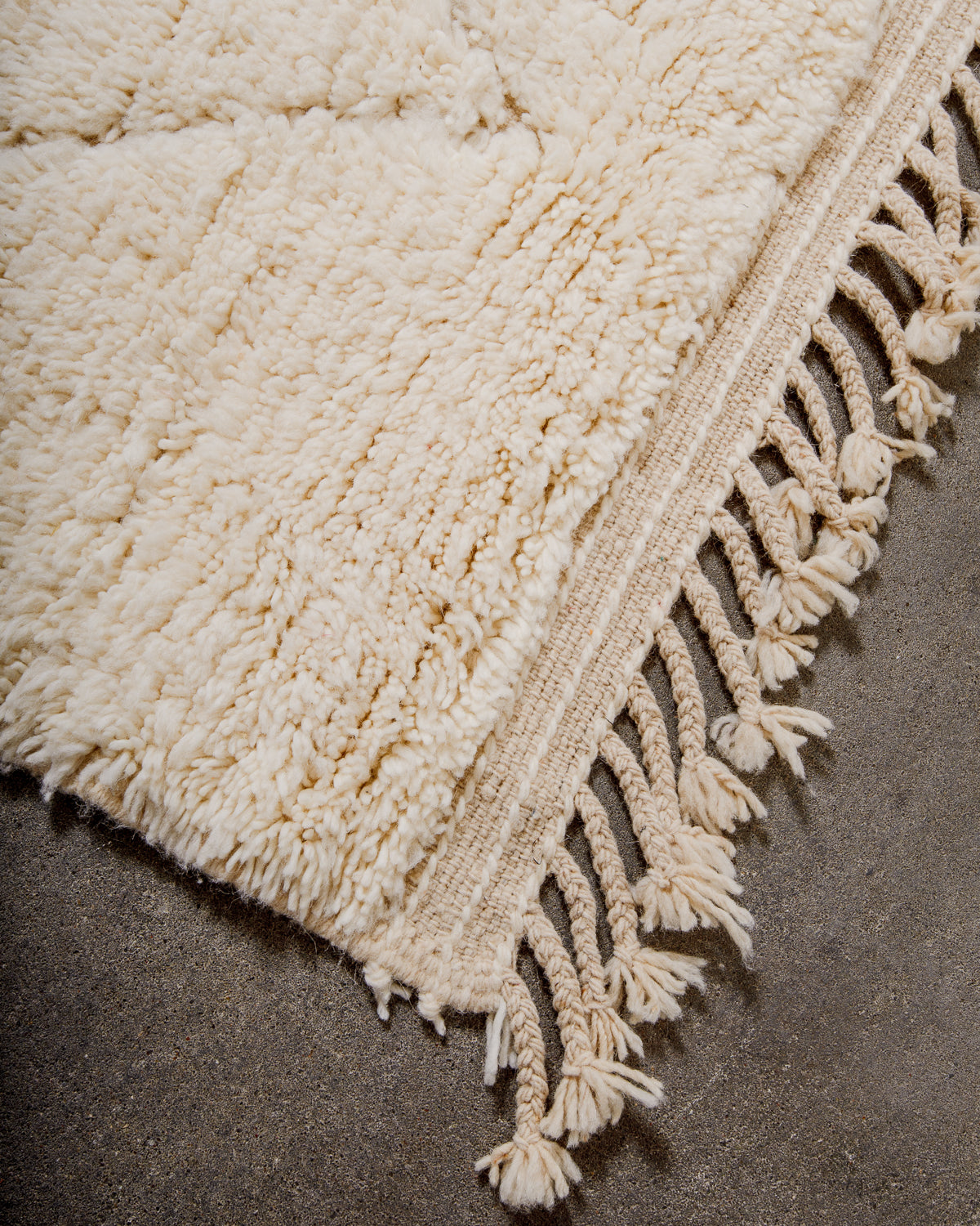 Corner of beniourain rug with tightly woven end and natural wool tassels.